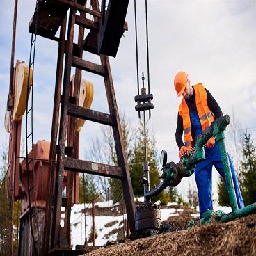 oil worker in orange uniform and helmet working with a pipe wrench near an oil pump jack